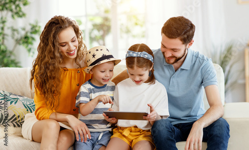 Cheerful parents with kids surfing tablet on couch at home