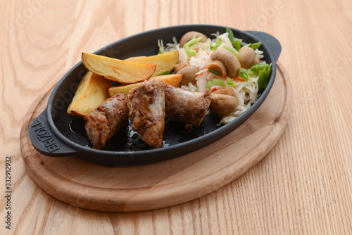 Grilled meat in mushroom's sauce and baked potato with cabbage mushroom salad in a pan on rustic wooden table.