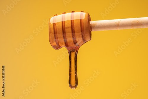 dripping sweet honey from wooden dipper on yellow background