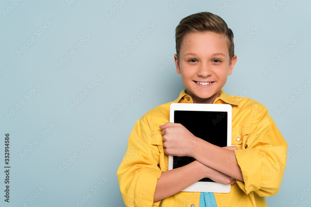 smiling kid holding digital tablet and looking at camera on blue background