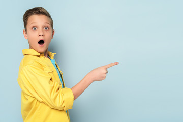 shocked and cute kid pointing with finger on blue background