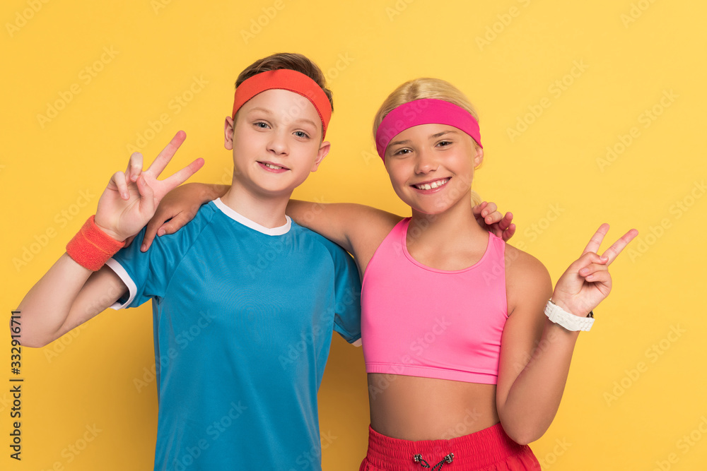 smiling kids in sportswear showing peace gesture on yellow background smiling kids in sportswear showing peace gesture on yellow background
