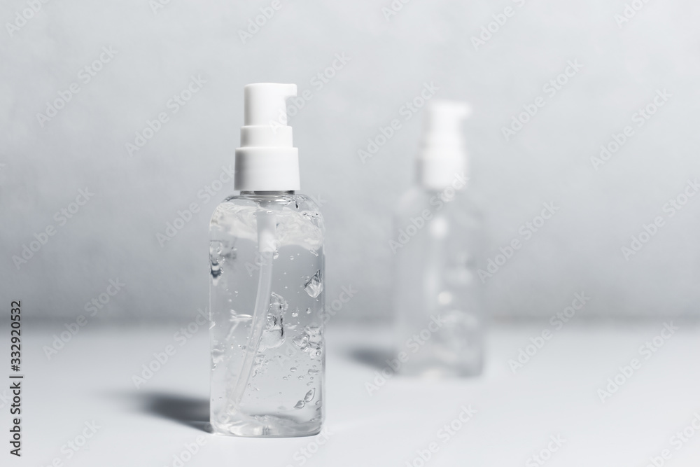 Close-up of two portable plastic bottles with sanitizer antiseptic gel on white table. Grey textured background.