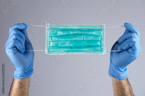 Dettaglio di una mascherina chirurgica tenuta da due guanti blu photo
