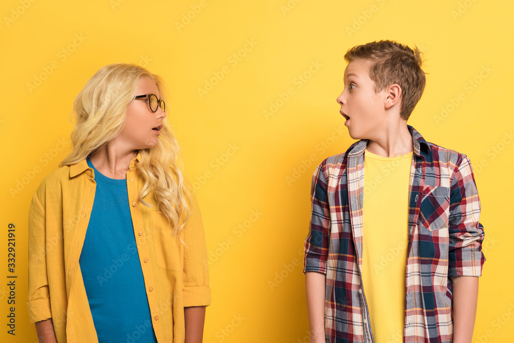 shocked kids looking each at other on yellow background shocked kids looking each at other on yellow background