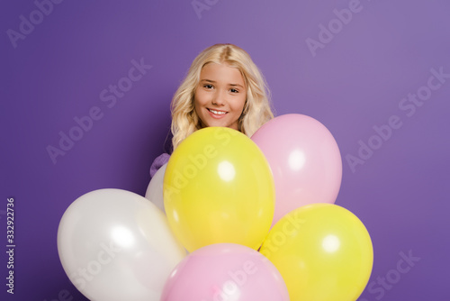 smiling kid with balloons looking at camera on purple background