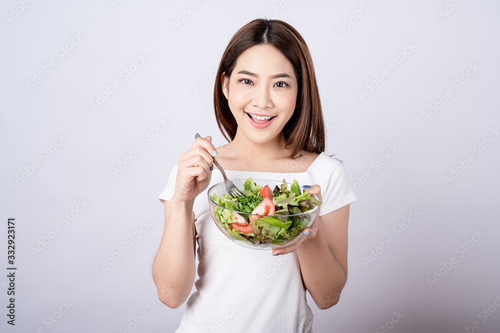 Beautiful young asian eating salad with big smile happy beaming face in seamless white isolated background. Diet healthy concept. Her face and skin are healthy, fresh, bright and youthful. Beautiful young asian eating salad with big smile happy beaming face in seamless white isolated background. Diet healthy concept. Her face and skin are healthy, fresh, bright and youthful.