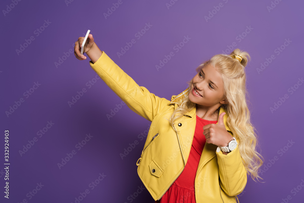 smiling kid taking selfie and showing like on purple background smiling kid taking selfie and showing like on purple background