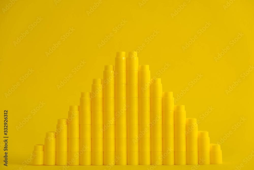Yellow plastic building blocks in the shape of a pyramid on yellow background. Background of plastic details building blocks. Parts of bright small spare parts for toys. Copy, empty space for text