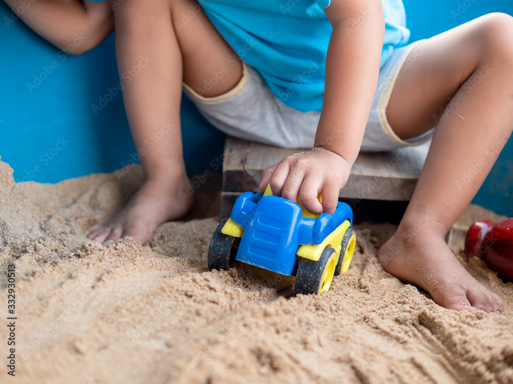 Asian little child boy hand playing car toy and sand in sandbox outdoor in natural background. Young kid in blue t-shirt in family relax and freedom time in summer holiday. Asian little child boy hand playing car toy and sand in sandbox outdoor in natural background. Young kid in blue t-shirt in family relax and freedom time in summer holiday.