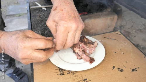 Old chef breaks ribs in his fingers and checks the cooked meat on a white plate. Tasting during the preparation of an excellent party dinner. photo