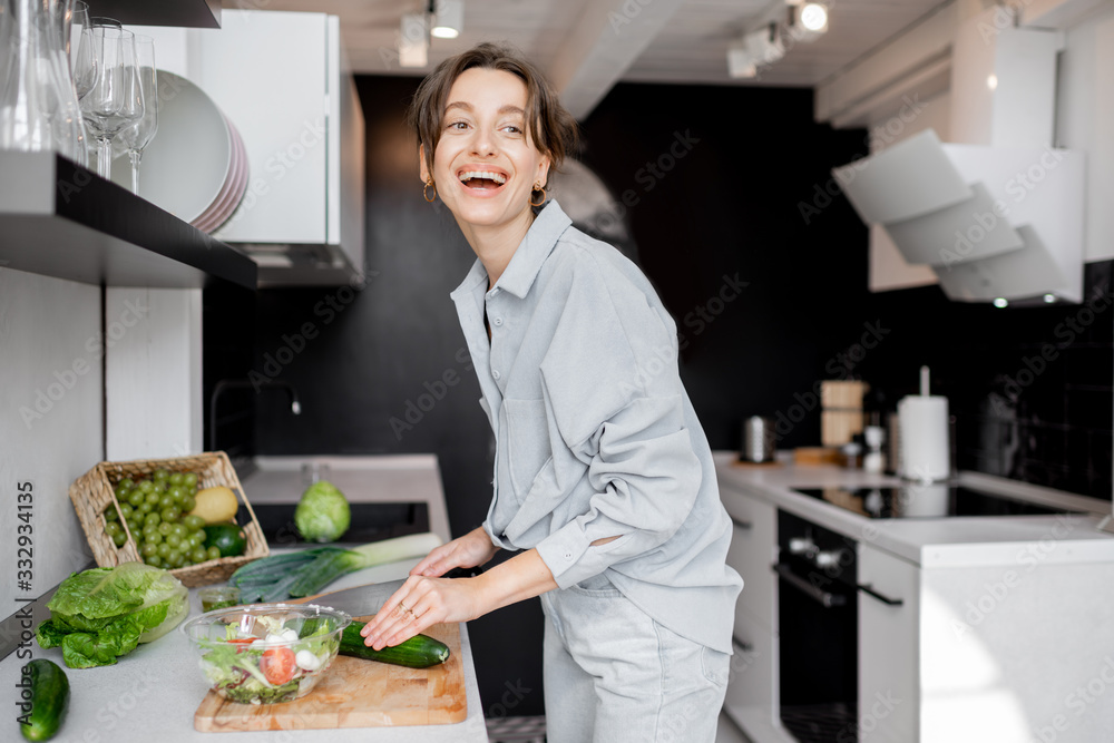 Young and cheerful woman cooking food with healthy vegetarian ingredients on the kitchen at home. Healthy eating, food and lifestyle concept Young and cheerful woman cooking food with healthy vegetarian ingredients on the kitchen at home. Healthy eating, food and lifestyle concept