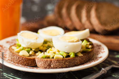 A glass of juice, sandwiches with avocado and egg, black whole grain bread. The concept of diet and proper nutrition