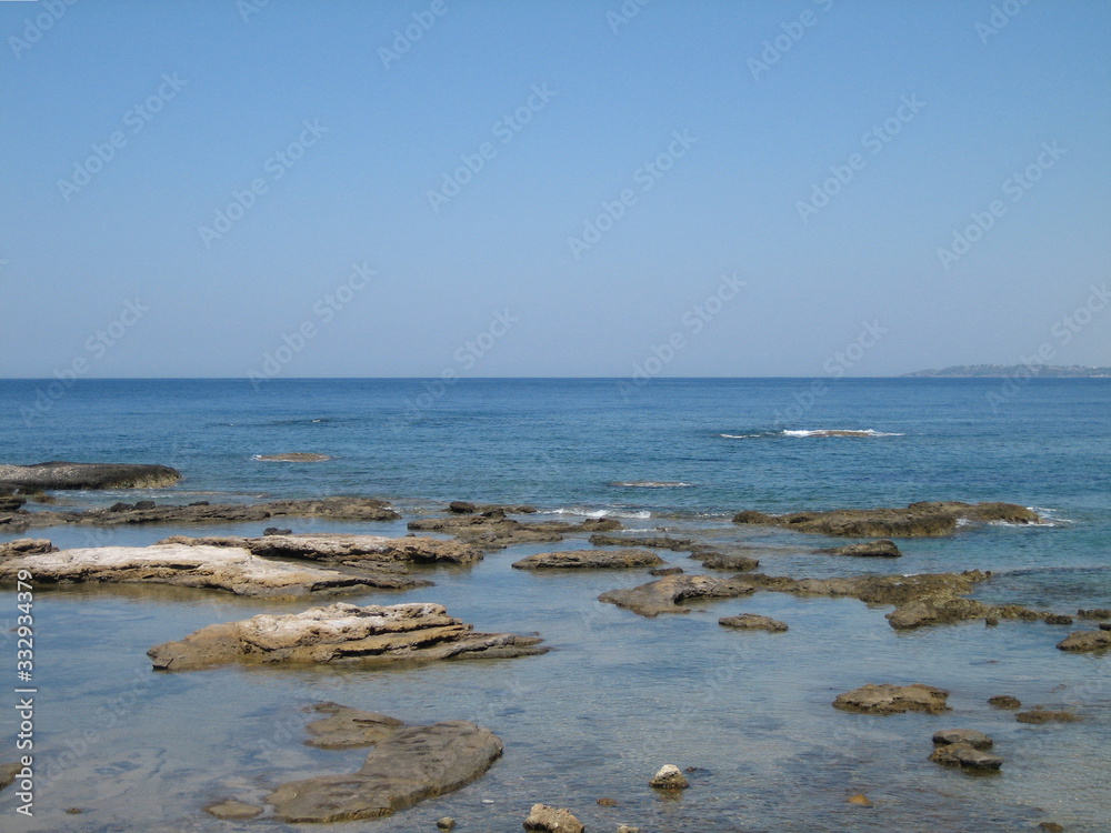 Weak waves gently wash the stones lying on the shallow bottom of the sea rocky shore in good weather.