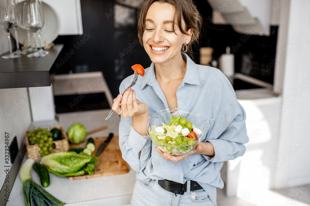 Portrait of a young and cheerful woman eating healthy salad on the kitchen at home. Healthy eating, food and lifestyle concept Portrait of a young and cheerful woman eating healthy salad on the kitchen at home. Healthy eating, food and lifestyle concept