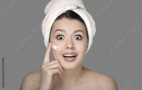 woman in towel smears cream on her face ￼