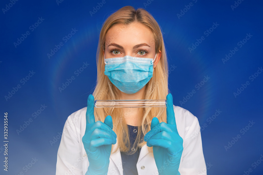A girl doctor in a medical mask and gloves holding test tube on a blue background A girl doctor in a medical mask and gloves holding test tube on a blue background