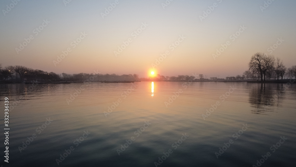 Epic wide angle shot of sun peaking up over lake inlet with empty boat docks in the early morning in Chicago Illinois