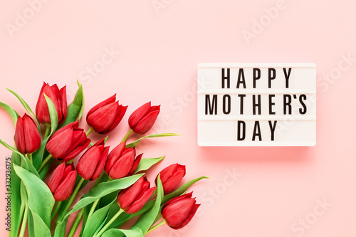 Mothers Day background. HAPPY MOTHERS DAY written in lightbox and bouquet of red tulips on pink background. Top view, copy space for text.