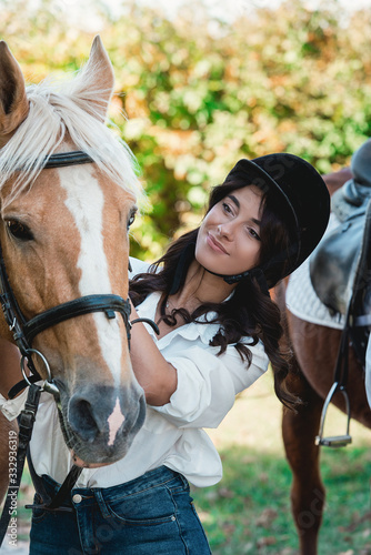 Portrait of young brunette woman in a white shirt and helmet near horse