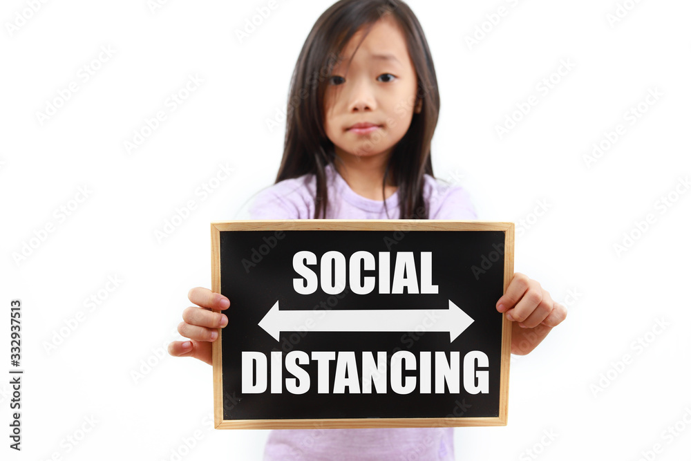 Portrait of little Asian girl holding a chalk board with text Social Distancing Portrait of little Asian girl holding a chalk board with text Social Distancing