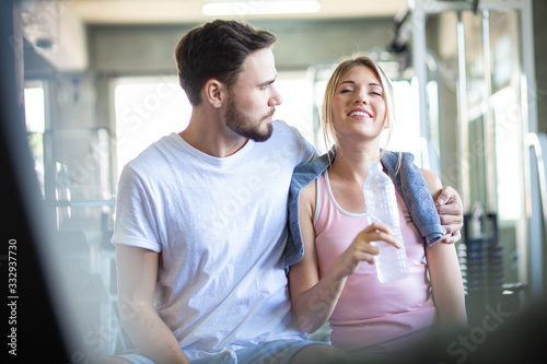 Young caucasian couple at gym talkign together and drinkking water after exercise.