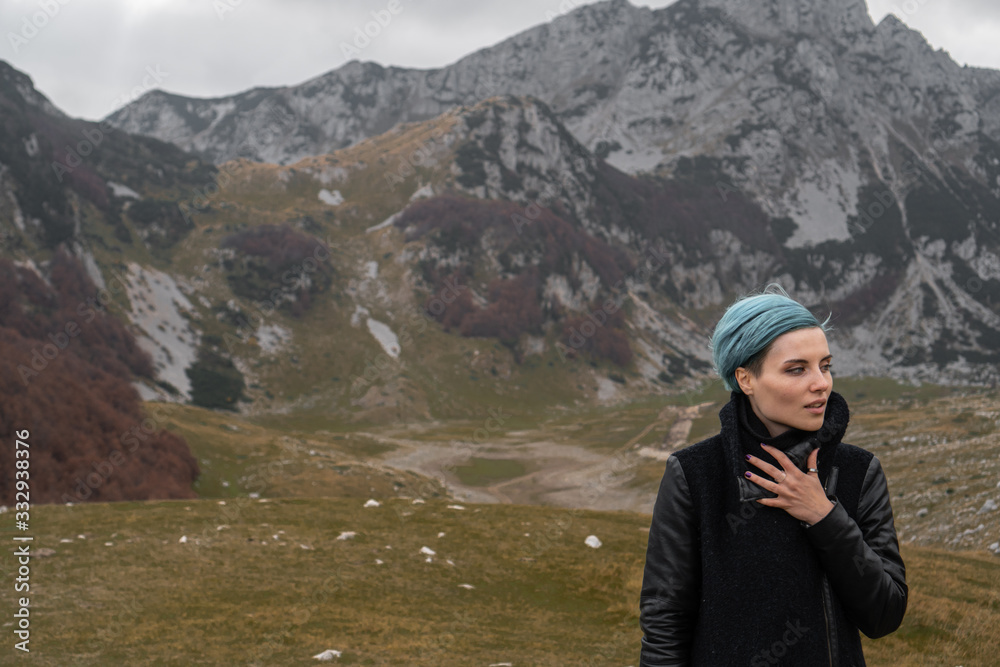 Naklejka premium A young woman with blue hair in a black coat walks on the mountainside