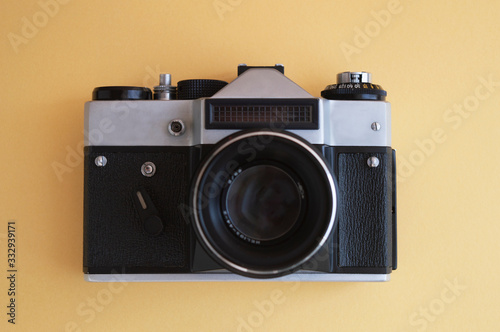 View from the top on vintage film photo camera on the yellow background. Metal silver and plastic black frame with lens.