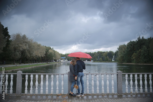 rain in the autumn park / young 25 years old couple man and woman walk under an umbrella in wet rainy weather, walk October lovers