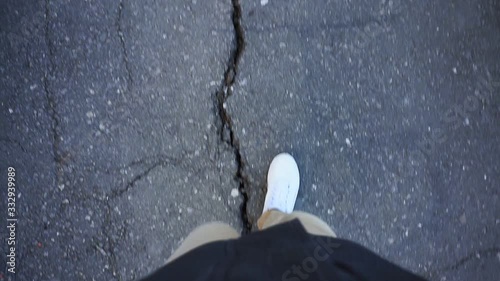 POV shot of a man's feet walking on the sidewalk with white sneakers in broad daylight. the old way, the crack on the pavement