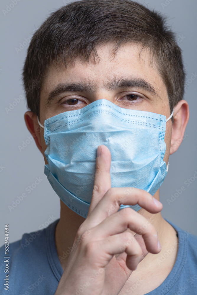 portrait of a man in a protective medical mask on face showing sign of silence gesture putting finger in mouth and lips, concept medical secrecy, moment of mourning and silence portrait of a man in a protective medical mask on face showing sign of silence gesture putting finger in mouth and lips, concept medical secrecy, moment of mourning and silence