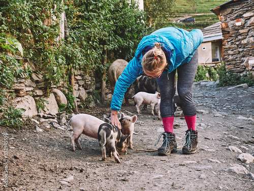 Blonde tourist girl petting small pigs on the street of Ushguli, Georgia
