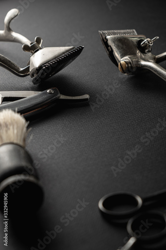 On a black surface are old barber tools. two vintage manual hair clipper, comb, razor, shaving brush, hairdressing scissors. black monochrome. vertical