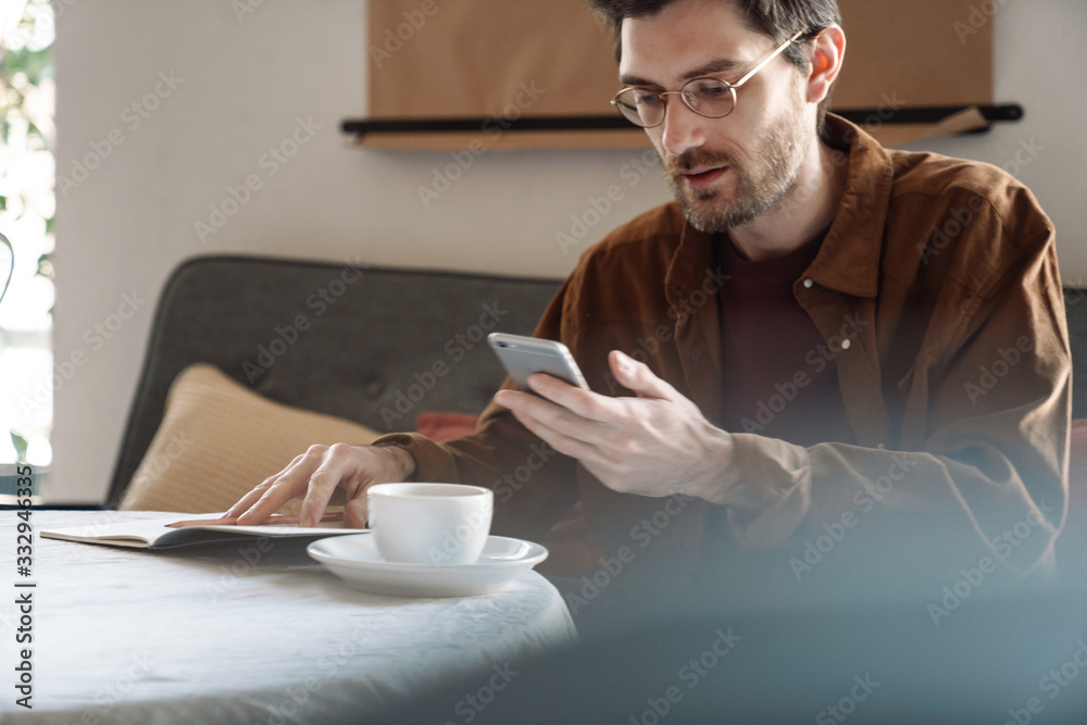 Image of handsome focused young man wearing eyeglasses using cellphone Image of handsome focused young man wearing eyeglasses using cellphone