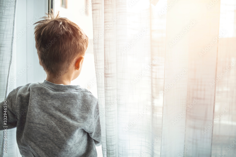 Boy sits on windowsill and looks out window, sitting home, wants to walk. Virus protection, coronavirus pandemic, prevention epidemic. Stay at home quarantine for coronavirus pandemic prevention. Boy sits on windowsill and looks out window, sitting home, wants to walk. Virus protection, coronavirus pandemic, prevention epidemic. Stay at home quarantine for coronavirus pandemic prevention.