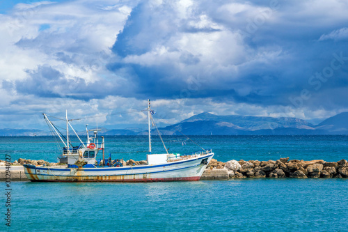 Beautiful landscape - sea bay with calm turquoise water, old fisher boat, stone breakwater, gray clouds on the sky and mountains on the horizon. 