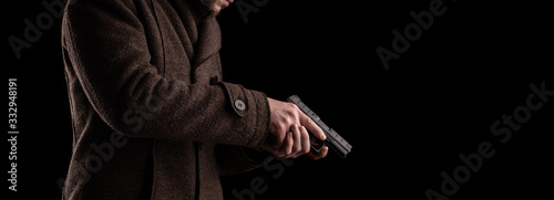 A man in a dark coat holds a gun. Security guard or bodyguard with arms in hand.