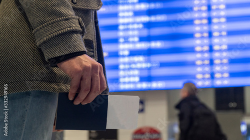 A man holds in his hand a passport with a plane ticket. Arrival schedule. Young guy at the airport. Waiting for your plane. Canceled flight. Boarding a plane. Traveler.