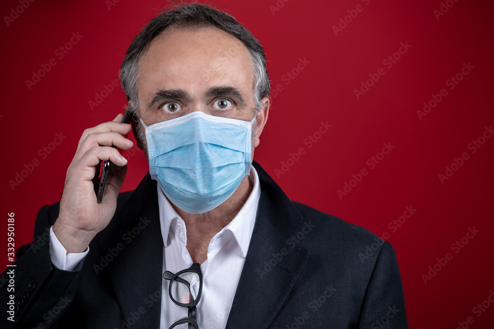 uomo in giacca e camicia indossa una mascherina eparla al suo cellulare, isolato su sfondo rosso uomo in giacca e camicia indossa una mascherina eparla al suo cellulare, isolato su sfondo rosso