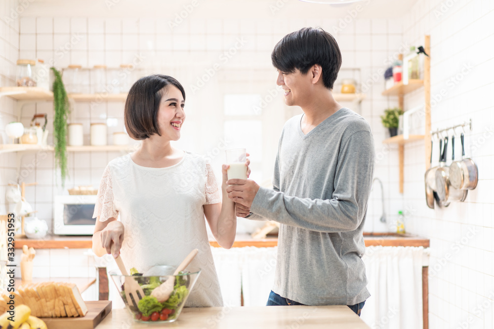 Asia new couple family stand in warm kitchen. Pregnant woman and husband hold glass of milk together. Girl cooks salad for man. They prepare healthy food in lovely home. Baby family pregnancy concept. Asia new couple family stand in warm kitchen. Pregnant woman and husband hold glass of milk together. Girl cooks salad for man. They prepare healthy food in lovely home. Baby family pregnancy concept.