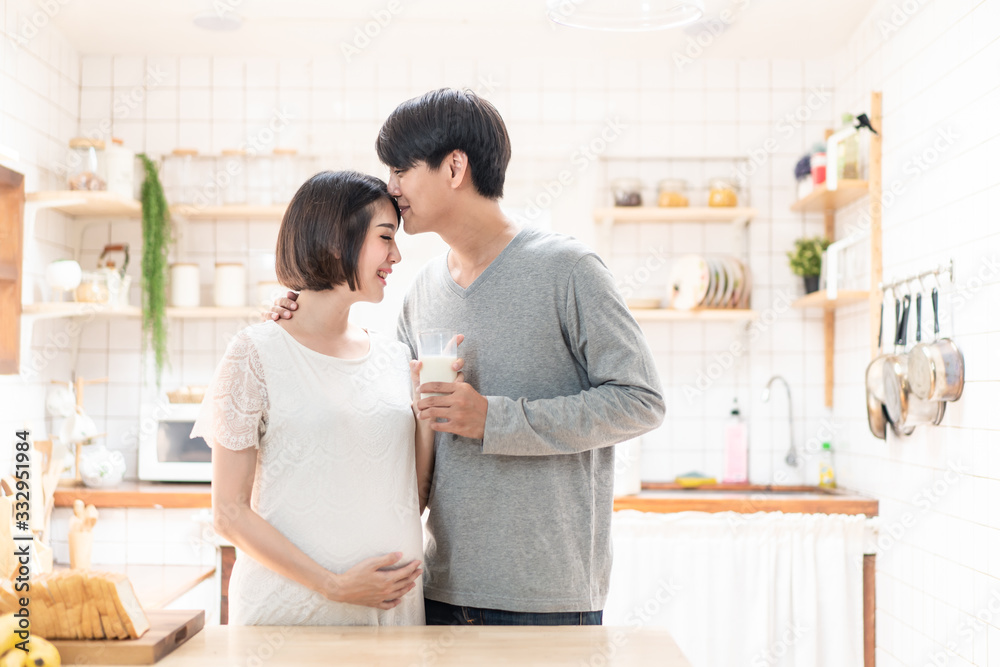 Asia new couple family stand in warm kitchen. Pregnant woman and husband hold glass of milk together. Girl cooks salad,prepare healthy food in lovely home. Man kiss wife. Baby family pregnancy concept Asia new couple family stand in warm kitchen. Pregnant woman and husband hold glass of milk together. Girl cooks salad,prepare healthy food in lovely home. Man kiss wife. Baby family pregnancy concept