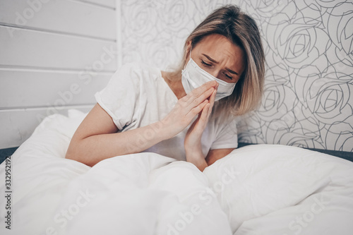 Young woman coughing in arms sick of coronavirus viral infection spreading corona virus covering mouth and nose. Painful cough ill patient lying in bed at home quarantine isolation. First symptoms