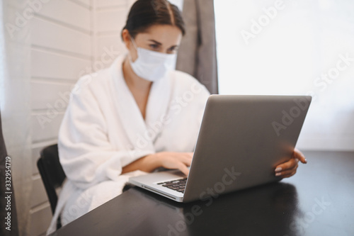 Sick woman in face medical mask working on a laptop during home quarantine isolation COVID-19 pandemic Corona virus. Distance online work from home concept. Coronavirus viral infection symptoms