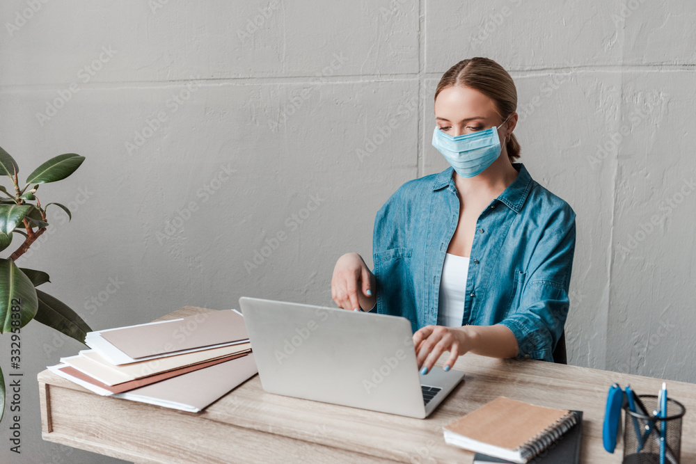 woman in medical mask working with laptop in office