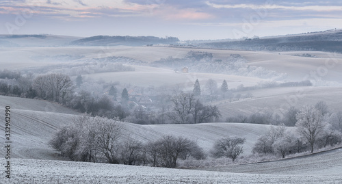 Obraz na płótnie Panoramic Rural Landscape With Wavy Plowed Fields, Trees In Hoarfrost And Old Windmill In Morning Fog. Winter Arable Land. Beautiful Frosted Cultivated Field. Frozen Grass. Christams In Moravia, Czech w salonie