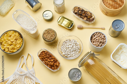 Creative flatlay with pantry staples. Glass jars with pasta, beans and chickpeas, canned goods, nuts and dried mushrooms in reusable containers. Top view pattern with basic products  photo
