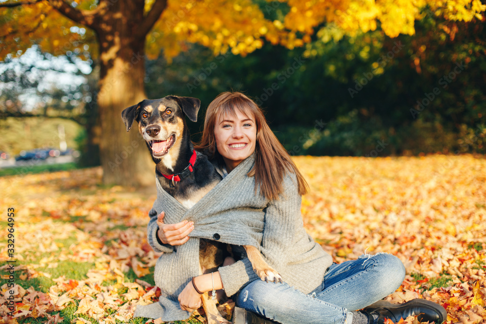 Happy young Caucasian woman sitting on ground hugging dog. Owner walking with pet on autumn fall day. Best friends having fun outdoor. Friendship of human with a domestic animal. Happy young Caucasian woman sitting on ground hugging dog. Owner walking with pet on autumn fall day. Best friends having fun outdoor. Friendship of human with a domestic animal.