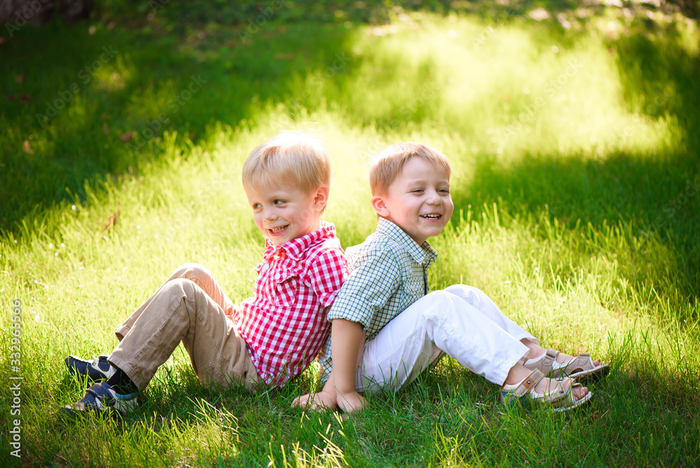 Fototapeta premium Two brothers are sitting on sunny glade in park