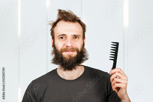 Young bearded shaggy man holding comb. For barbershop.