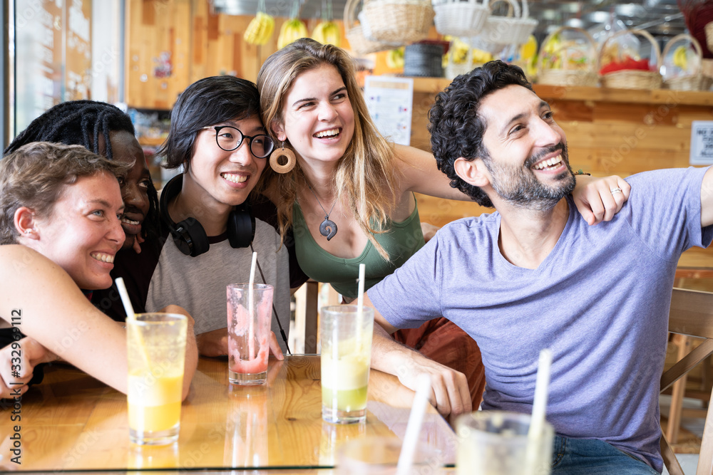 Group people from different ethnicities making a selfie with a mobile sitting and drinking fruit juices in a bar Group people from different ethnicities making a selfie with a mobile sitting and drinking fruit juices in a bar